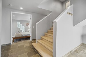 A modern interior with a staircase, a bed with a white headboard, and a wall-mounted light fixture. - Luxury 6 bedroom Oceanfront Hollywood Beach Mansion (Oxnard)