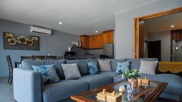 A modern living room with a grey sofa, wooden coffee table, and a dining area with a kitchen in the background.