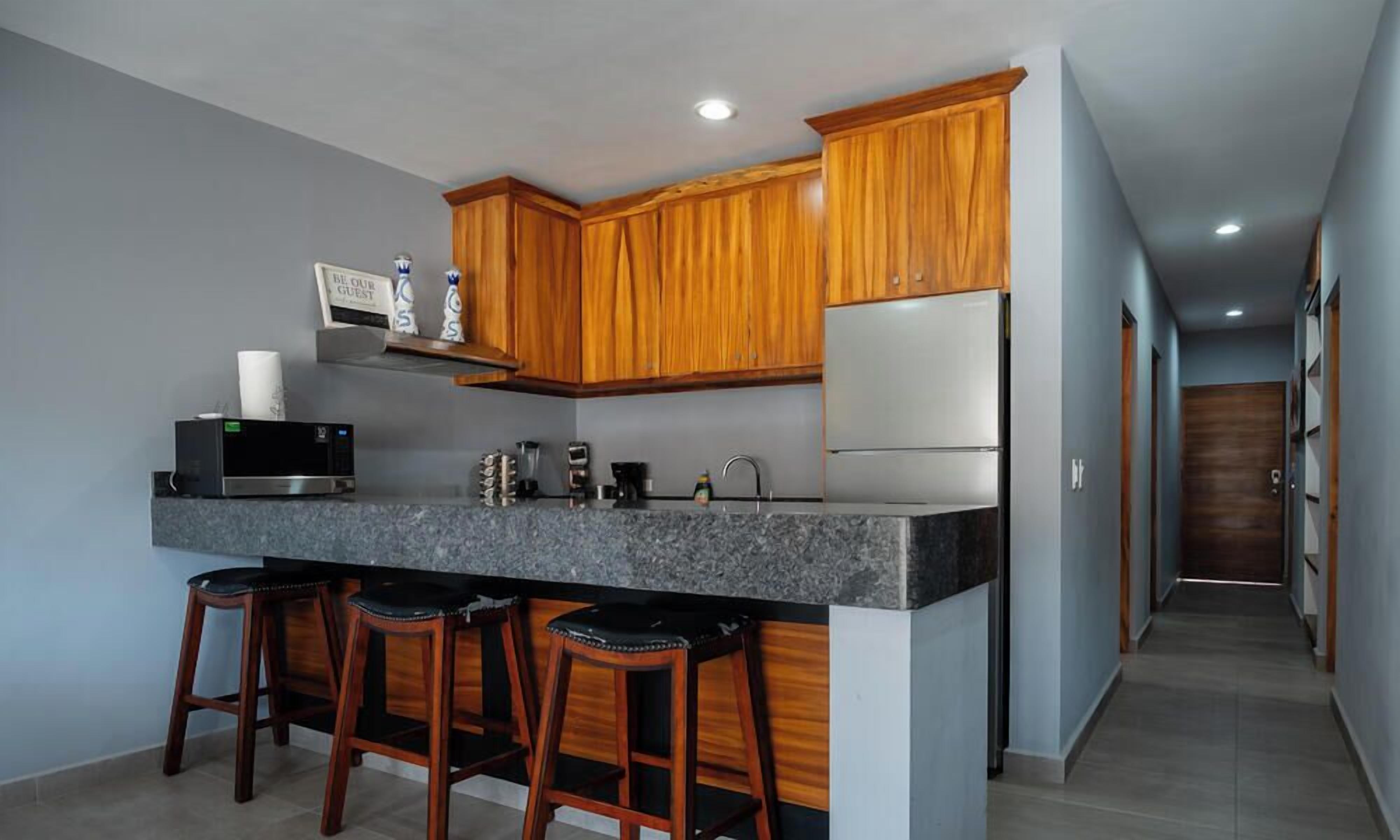 A kitchen with wooden cabinets, a granite countertop, a stainless steel refrigerator, and a built-in microwave.