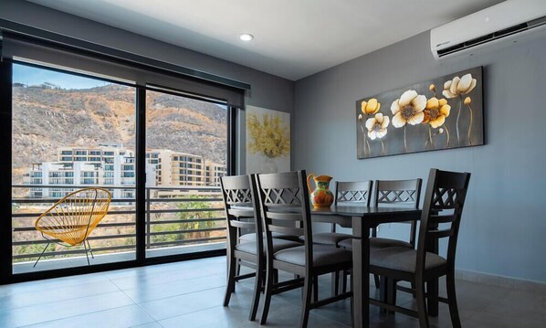 Un comedor con una mesa y sillas, una ventana que ofrece vistas a edificios y un cuadro en la pared.