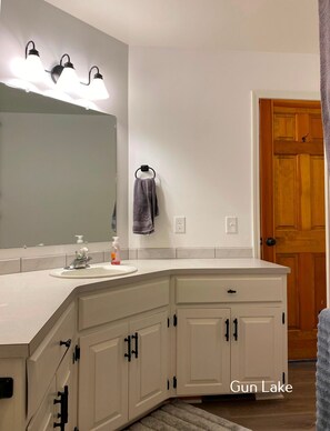 Un baño moderno con un amplio tocador, un espejo y tres luces fijadas a la pared.