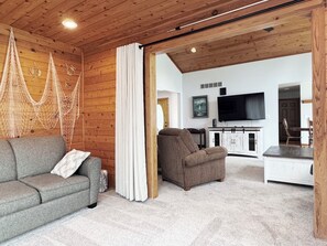 A cozy living room with a grey sofa, a brown armchair, and a TV mounted on the wall. - Gun lake 4 Bed 2.5 Bath Home w/2 car garage, kayaks, paddleboards, free Wi-Fi (Wayland)