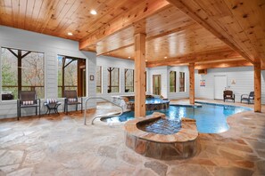 An indoor swimming pool area with stone flooring, wooden beams, and seating by the windows.