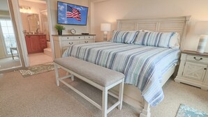 A bedroom with a bed, a bench, a nightstand, a dresser, a mirror, and a TV displaying an American flag. - New Listing! Beautiful 2000 Square Foot Multi-Level Townhome. 1 BLOCK FROM BEACH (Seaside Heights)