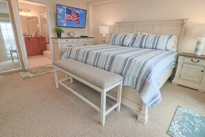 A bedroom with a bed, a bench, a nightstand, a dresser, a mirror, and a TV displaying an American flag.