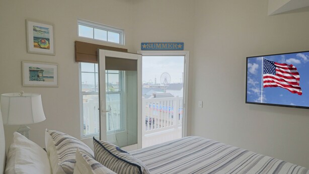 A bedroom with a bed, pillows, a lamp, a wall-mounted TV, and a balcony door. - New Listing! Beautiful 2000 Square Foot Multi-Level Townhome. 1 BLOCK FROM BEACH (Seaside Heights)