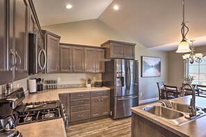 A modern kitchen with dark wood cabinets, stainless steel appliances, and a large island with a sink. - Rapid City Home w/ Patio < 5 Mi to Downtown! (Rapid City)