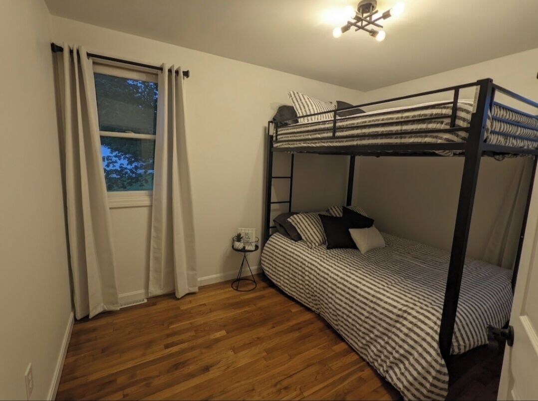 Dormitorio con literas, ventana, suelo de madera y una mesita con una planta.