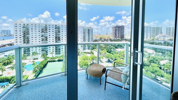Ein Balkon mit Blick auf hohe Gebäude, einen Pool und viel Grün.
