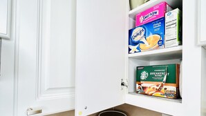 Eine Küche mit einem weißen Schrank, der eine Kaffeemaschine, einen Wasserkocher und eine Packung Kaffeekapseln enthält.