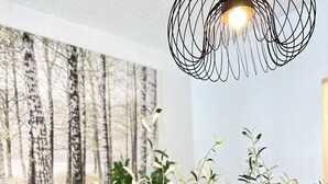 Ein Essbereich mit einem langen Tisch, gedeckt für vier Personen, mit gewebten Tischsets, klarem Glas und einer Vase mit Grünpflanzen.
