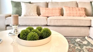 Ein Wohnzimmer mit einem beigefarbenen Sofa, dekorativen Kissen, einem weißen Couchtisch mit einer Zimmerpflanze und abstrakter Kunst an der Wand.