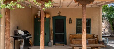 A rustic outdoor patio with a wooden grill, a green door, and a wooden bench.