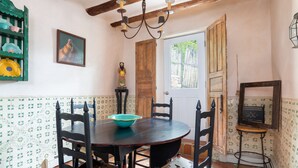 Un coin repas avec une table et des chaises en bois, une étagère verte où sont rangées de la vaisselle, une porte en bois et une petite table avec un miroir.
