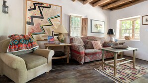Un salon chaleureux avec un plafond en bois, un canapé à motifs, une petite table avec une lampe et un grand tableau abstrait accroché au mur.