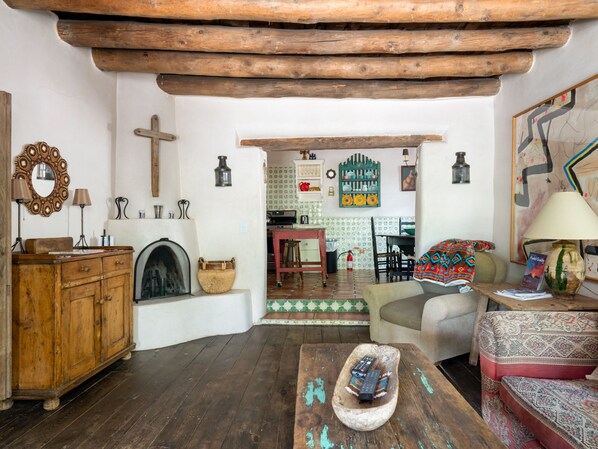 A cozy living room with wooden furniture, a fireplace, and a view into the kitchen. - El Nido Lane Tesuque by Kokopelli Property Management (Santa Fe)
