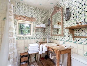 A bathroom with a wooden vanity, a sink, a toilet, and a window. There are towels stacked on a shelf and a mirror above the sink. - El Nido Lane Tesuque by Kokopelli Property Management (Santa Fe)