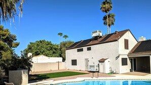 Ein Garten mit Swimmingpool, Liegestühlen, einem weißen Haus und Palmen.