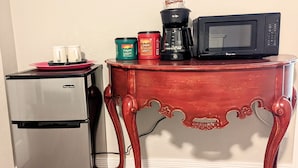 Eine kompakte Küche mit Kühlschrank, Mikrowelle, Kaffeemaschine und einem Tisch mit dekorativen Beinen.