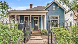 A two-story house with a curved front porch, a central entrance, and a small front yard with a metal fence.