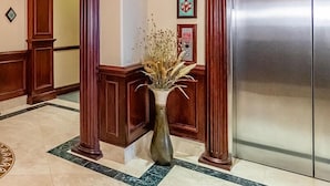 Un hall d’entrée doté d’un sol en marbre, de colonnes en bois, d’un grand ascenseur et d’un vase contenant des plantes séchées.