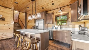 Une cuisine moderne avec des murs en bois, un îlot central doté de tabourets, des appareils en acier inoxydable et une fenêtre offrant une vue agréable.
