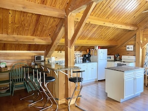 A rustic wooden interior with a kitchen area featuring a bar with stools, a refrigerator, and a microwave.