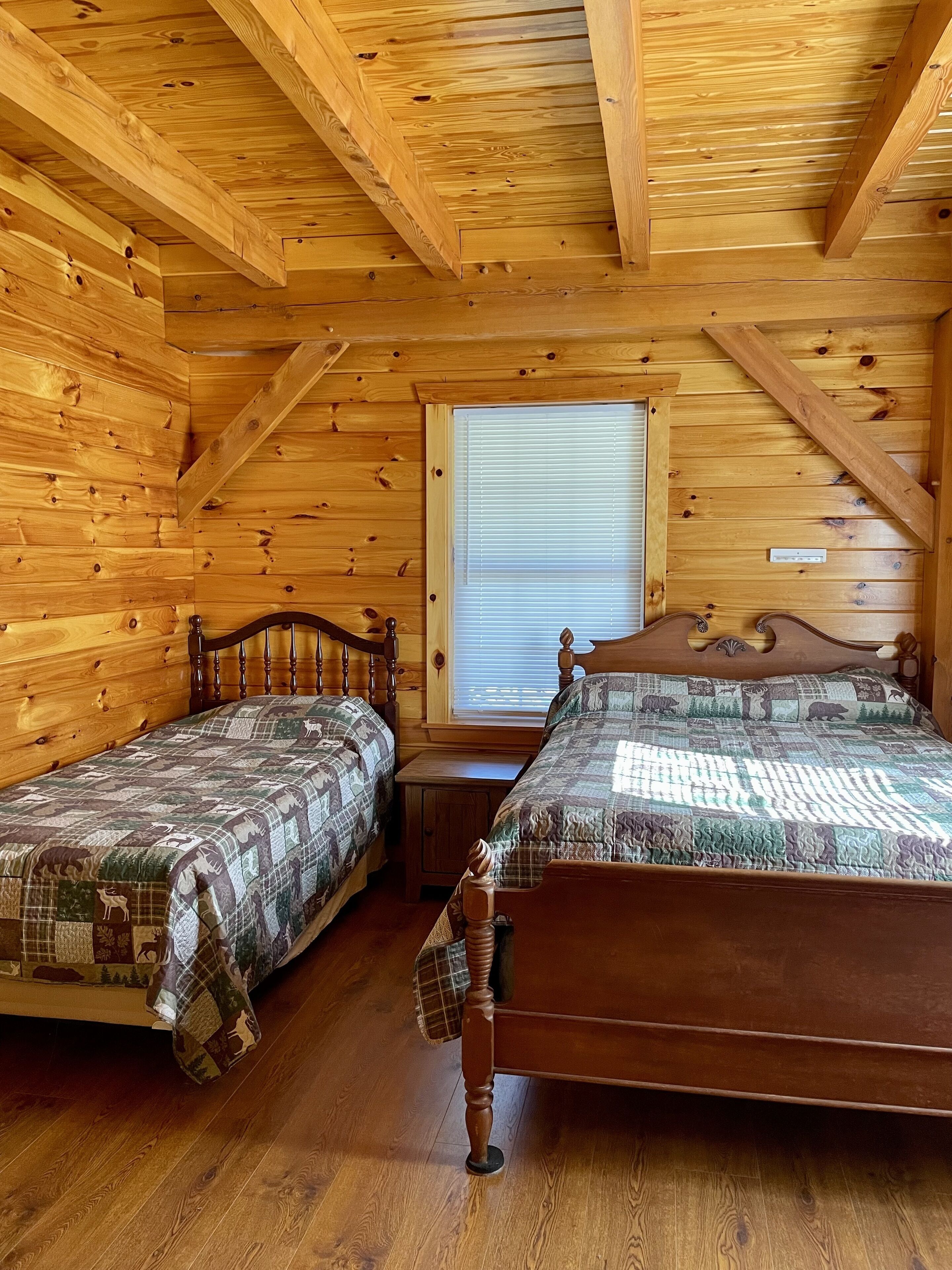 Un dormitorio tipo cabaña con dos camas de madera, una ventana con persianas y techo de madera.