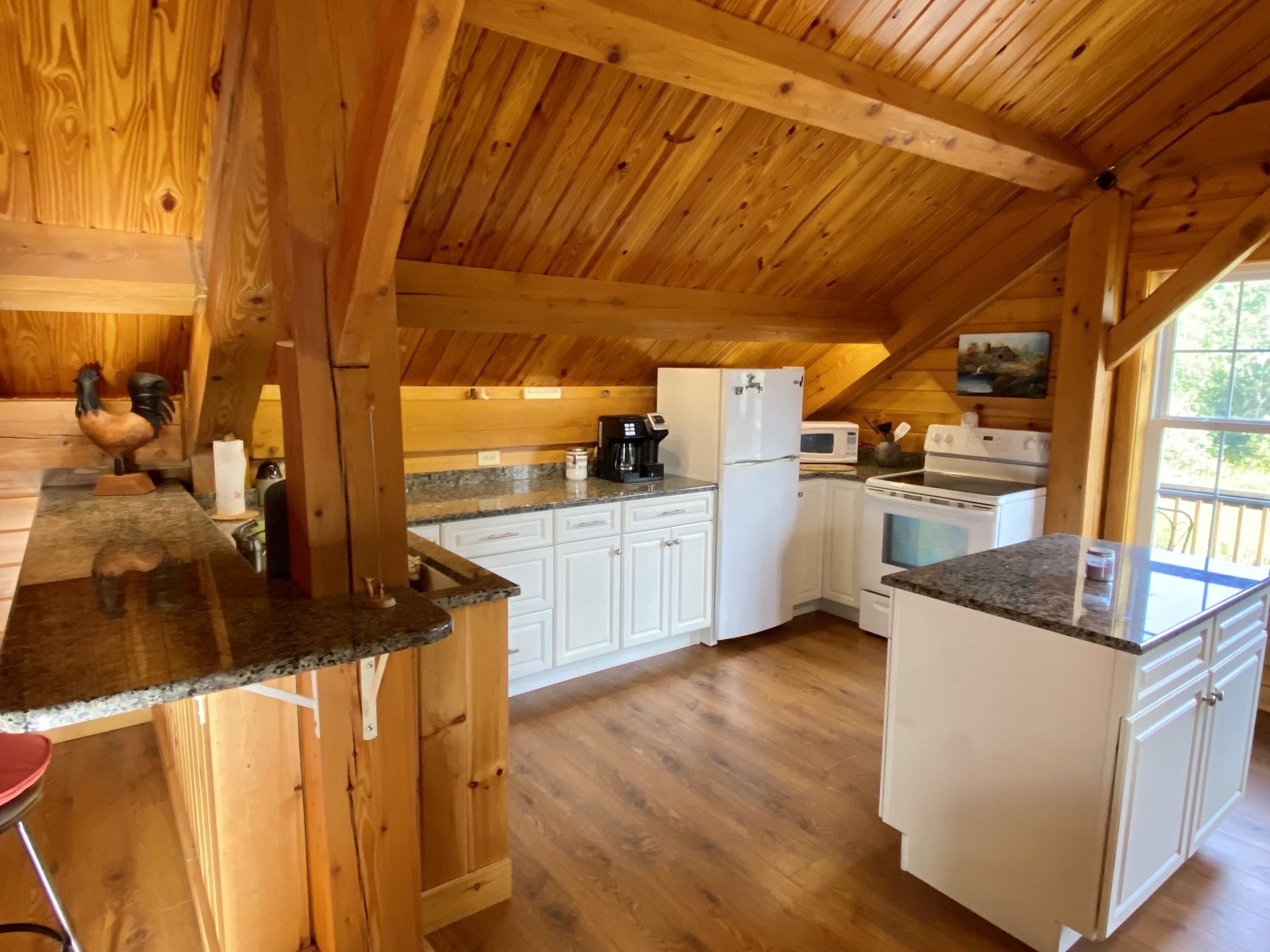 A wooden interior with a kitchen area featuring white cabinets, granite countertops, and a wooden ceiling.