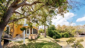 Ein gelbes Haus mit einer Hängematte, einer Terrasse mit Stühlen und einem kleinen Teich.