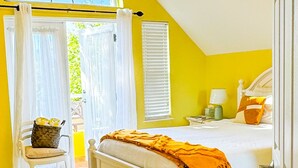 Ein Schlafzimmer mit Bett, Deckenventilator, Fenster mit Vorhängen und Blick ins Freie.