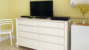 Ein Zimmer mit einem weißen Schminktisch, einem weißen Stuhl, einem kleinen Tisch mit einer Vase und einer Wand-Klimaanlage.