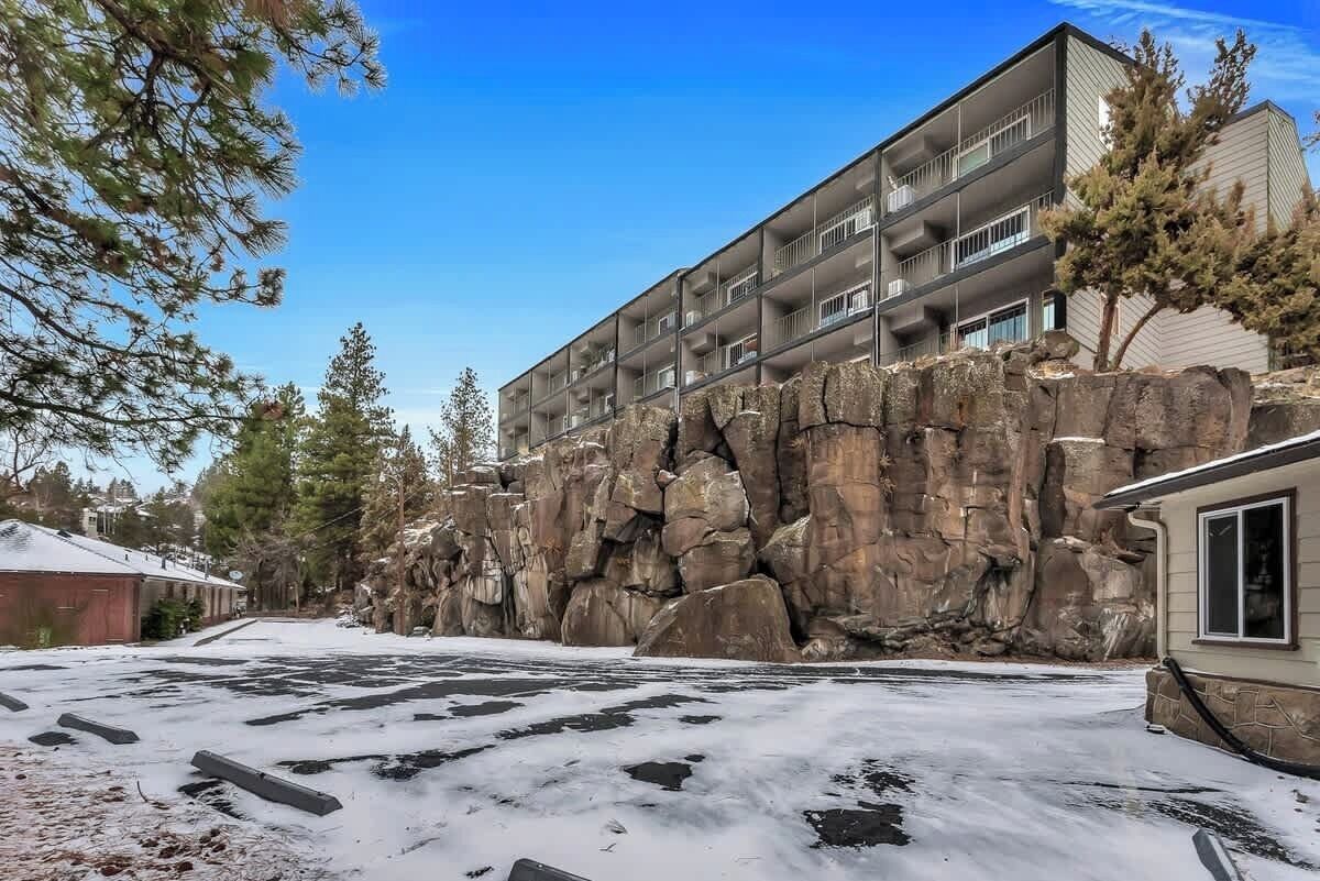 A multi-story building with balconies, a snow-covered ground, and a rocky cliff.