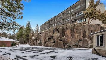 A multi-story building with balconies, a snow-covered ground, and a rocky cliff.