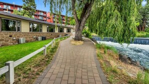 A pathway leading to a building with a stone facade, a weeping willow tree, and a river.