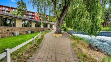 A pathway leading to a building with a stone facade, a weeping willow tree, and a river.