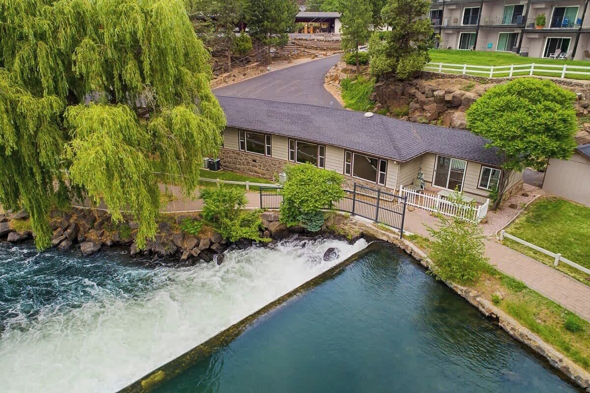 A riverside hotel with a waterfall, a stone bridge, and a well-maintained lawn.