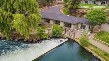 A riverside hotel with a waterfall, a stone bridge, and a well-maintained lawn.