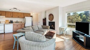 A modern living room with a sofa, coffee table, TV, fireplace, and kitchen area.