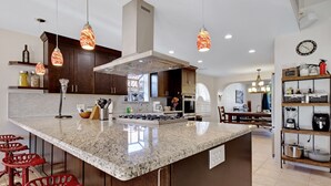 Une cuisine moderne dotée de plans de travail en granit, d’appareils électroménagers en acier inoxydable et de luminaires suspendus.