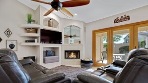 Un salon avec des canapés en cuir, une cheminée, un ventilateur de plafond et une vue sur l’extérieur.