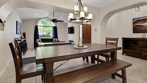 Un espace repas comprenant une grande table en bois, des chaises, un lustre et un ventilateur de plafond.