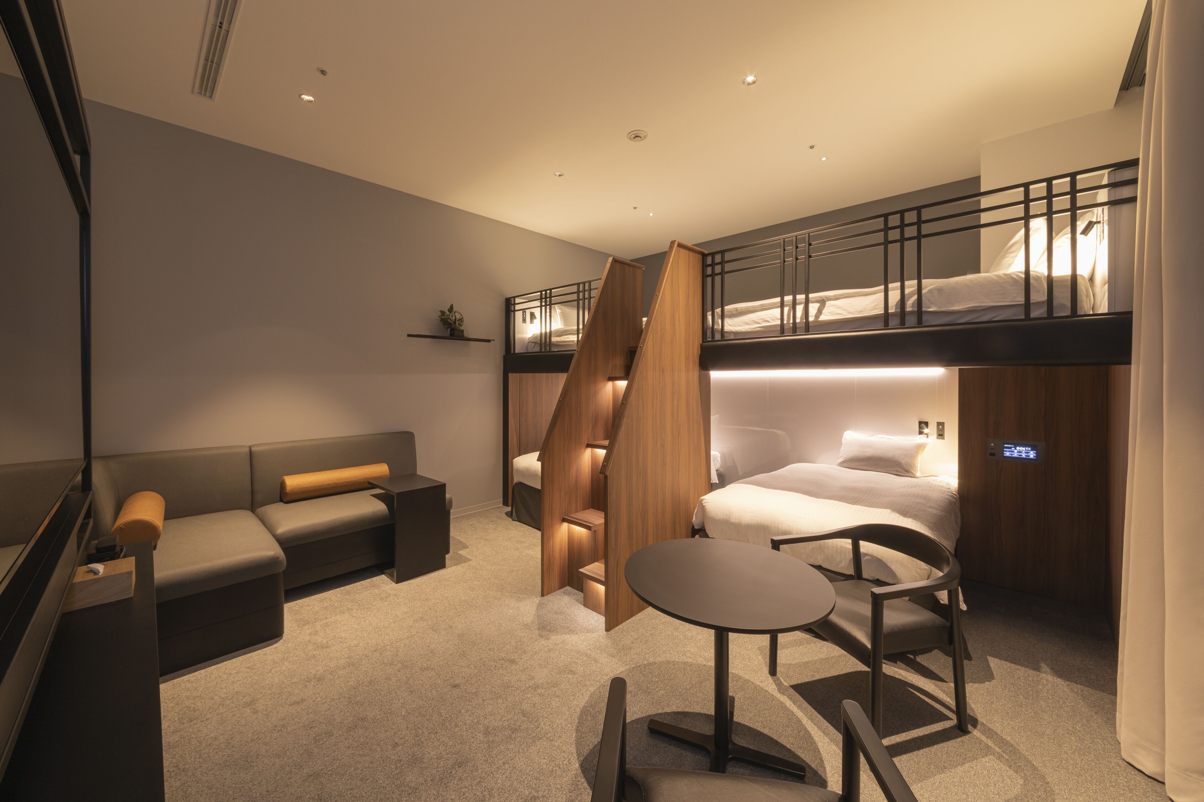 Una habitación de hotel moderna con una cama litera, un sofá, una mesita pequeña y un escritorio.