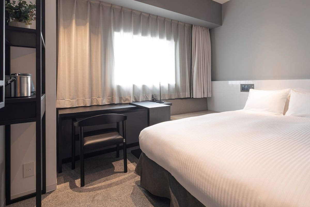 Een hotelkamer met een bed, een bureau, een stoel en een raam met gordijnen.
