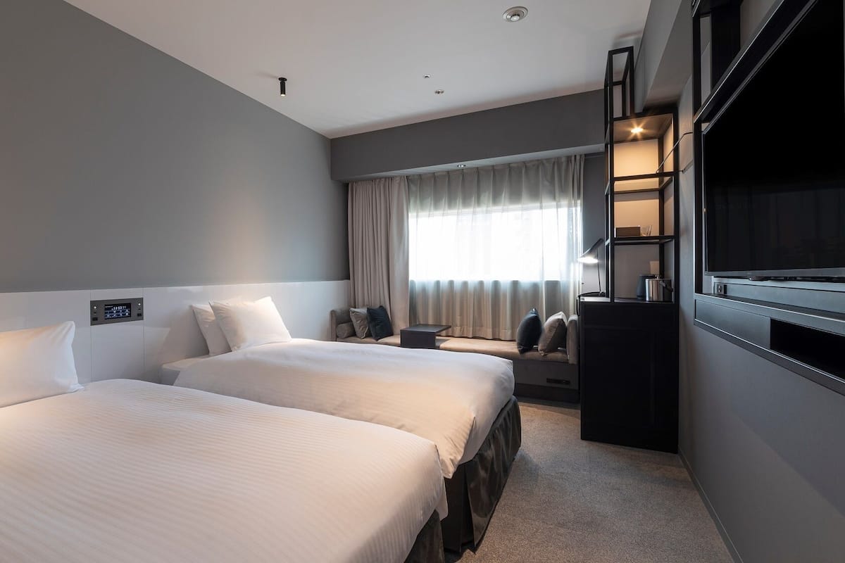 Een hotelkamer met twee bedden, een televisie, een bureau en een raam met gordijnen.
