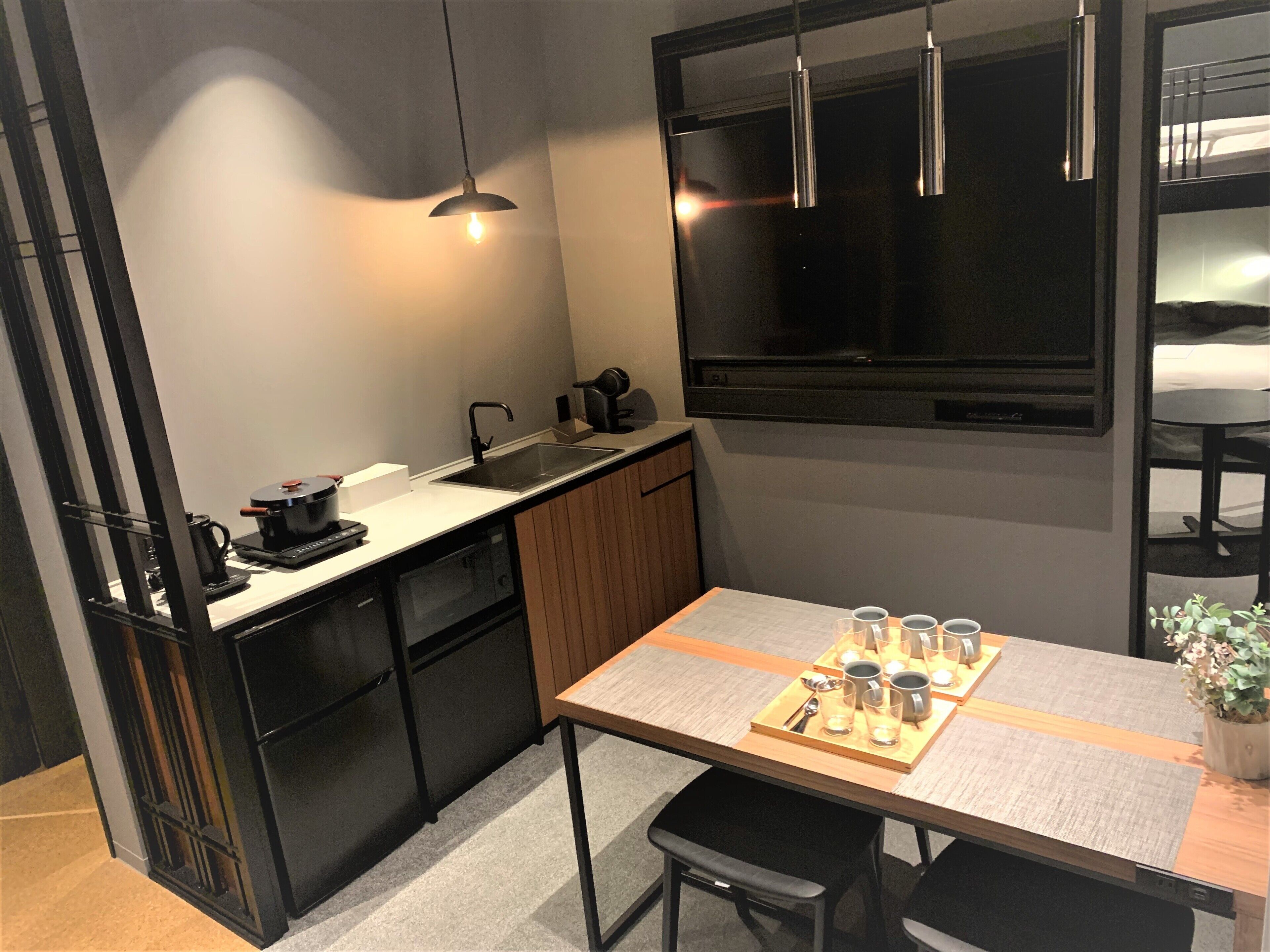 A compact kitchen with a modern design, featuring a black countertop, a built-in oven, and a small sink. There is a dining area with a table set for two, including glasses and cutlery.