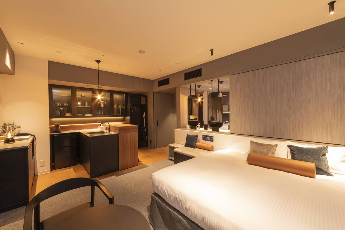 Une chambre d’hôtel moderne dotée d’un grand lit, d’un coin salon séparé, d’une kitchenette et d’une salle de bain.