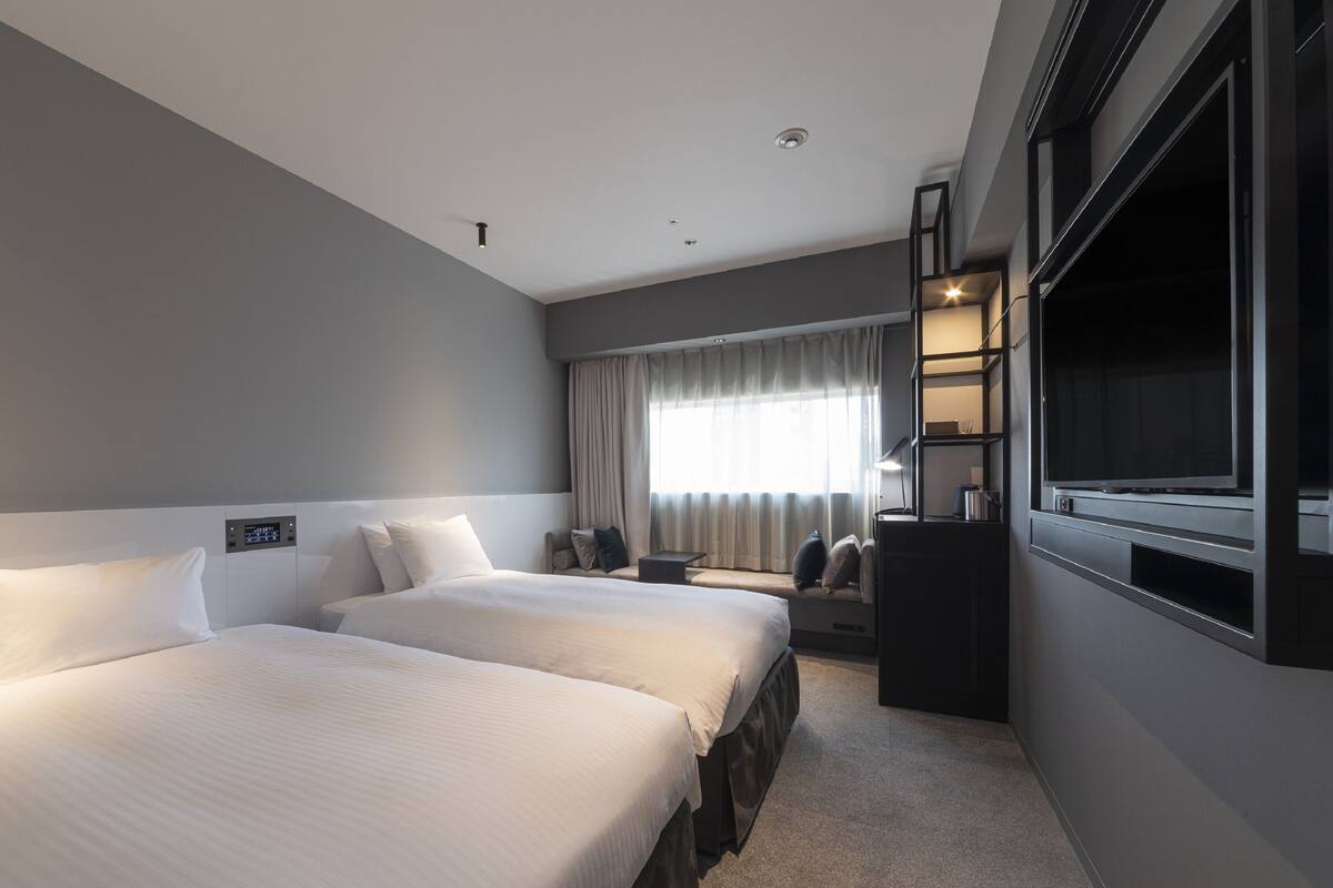 Une chambre d’hôtel avec deux lits, un bureau, une télévision et une fenêtre avec des rideaux.
