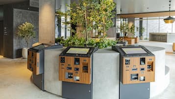 Uma área de recepção moderna com um jardim vertical central, dois quiosques de madeira e um balcão de pedra.