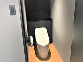 A compact, modern bathroom with a white toilet, a black partition, and a beige floor.